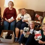 eight women in living room with sock collection for veterans