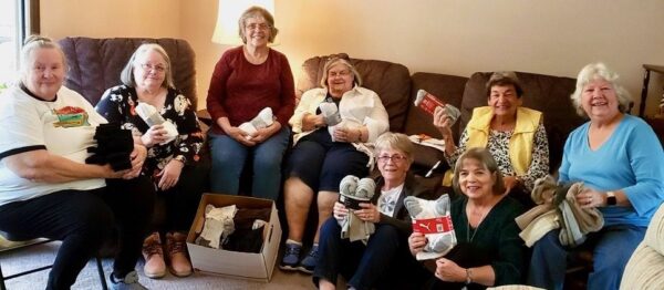 eight women in living room with sock collection for veterans