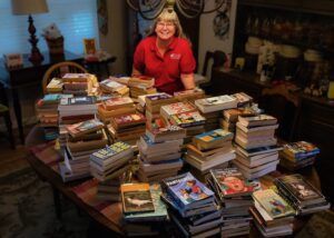woman standing with dozens of books stacked on a table