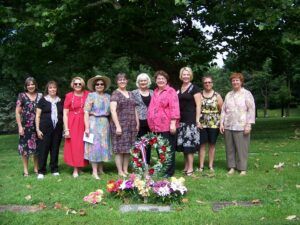 group of smiling women around a grave marker wreath and flowers